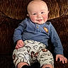 baby, child, infant, smiling, portrait, sitting, indoor, couch, upholstery, blue_sweater, football_pants, sportswear, black_socks, clothing, face, eyes, hands, happy, casual, photography