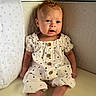 baby, infant, child, polka_dot, clothing, crib, pillow, star_pattern, curly_hair, blue_eyes, sitting, neutral_colors, wooden_buttons, cute, nursery, soft_lighting, portrait, indoors, expression, young