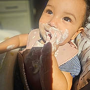 Olive joined the competition — help win amazing prizes! baby, child, food, bib, highchair, face, hand, smile, messy, indoor, light, shadow, curly_hair, skin, clothing, feeding, cute, closeup, happy, infant