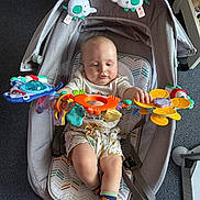 Jaxson is registered to the contest to win money with this photo: baby, baby_rocker, baby_seat, baby_toys, carpet, child, colorful_toy, cute, floor, indoor, infant, nursery, playing, plush_elephant, seated, shorts, socks, soft_lighting, toy, white_shirt