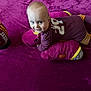 baby, blanket, child, clothing, cute, dinosaur, football, happy, indoor, infant, lying_down, maroon, person, play, plush_toy, purple, smile, socks, soft_toy, toy