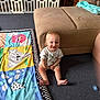 animal_print, baby, baby_gate, carpet, child, clothing, couch, cute, footwear, furniture, happy, home, indoor, infant, pacifier, person, play_mat, sitting, smiling, toy