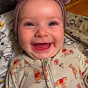 Willow is registered to the contest to win money with this photo: baby, smiling, face, headwear, bow, pajamas, winnie_the_pooh, blanket, pattern, happy, tongue, teeth, infant, child, cute, indoors, wood_floor, closeup, person, cozy