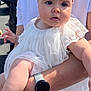 baby, child, infant, headband, white_dress, arm, watch, person, outdoor, sunlight, curious, holding, adult, face, skin, clothing, portrait, people, daylight, expression