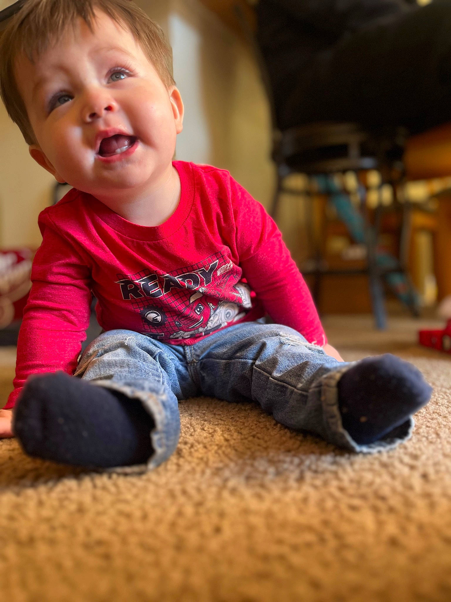 Mateo is registered to the contest to win money with this photo: baby, baby_toddler_clothing, cheek, child, face, floor, flooring, fun, happy, hardwood, human_leg, nose, person, play, sitting, skin, sleeve, smile, t_shirt, toddler