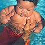 baby, child, pool, water, swimming, curly_hair, orange_shorts, hands, sunlight, reflection, skin, outdoor, summer, cute, holding, infant, person, swimwear, closeup, playful