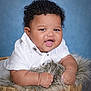 baby, child, smiling, curly_hair, basket, fuzzy_cushion, white_shirt, portrait, indoor, cute, happy, infant, skin, face, hands, background, studio, expression, person, closeup