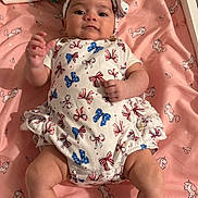 Celestial is registered to the contest to win money with this photo: baby, infant, onesie, headband, blanket, unicorn_pattern, pink, white_clothing, red_bows, blue_bows, lying_down, hand_raised, indoor, cute, child, face, person, soft_toys, sleeping_area, baby_accessories