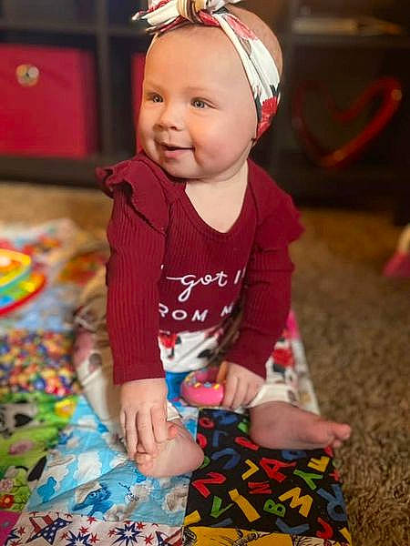 Lyra is registered to the contest to win money with this photo: baby, baby_toddler_clothing, child, eye, face, facial_expression, fashion_accessory, flooring, fun, grass, happy, head, headband, human_body, iris, pattern, person, sitting, skin, smile