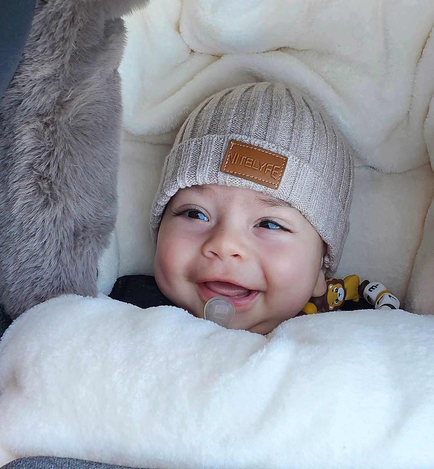 élias a rejoint le concours — aidez-le/la à gagner de superbes lots ! baby, smiling, hat, knit_hat, blanket, cozy, infant, cute, soft_texture, toy, lion_toy, face, happy, child, warm, sleeping_bag, cuddly, indoors, portrait, pacifier