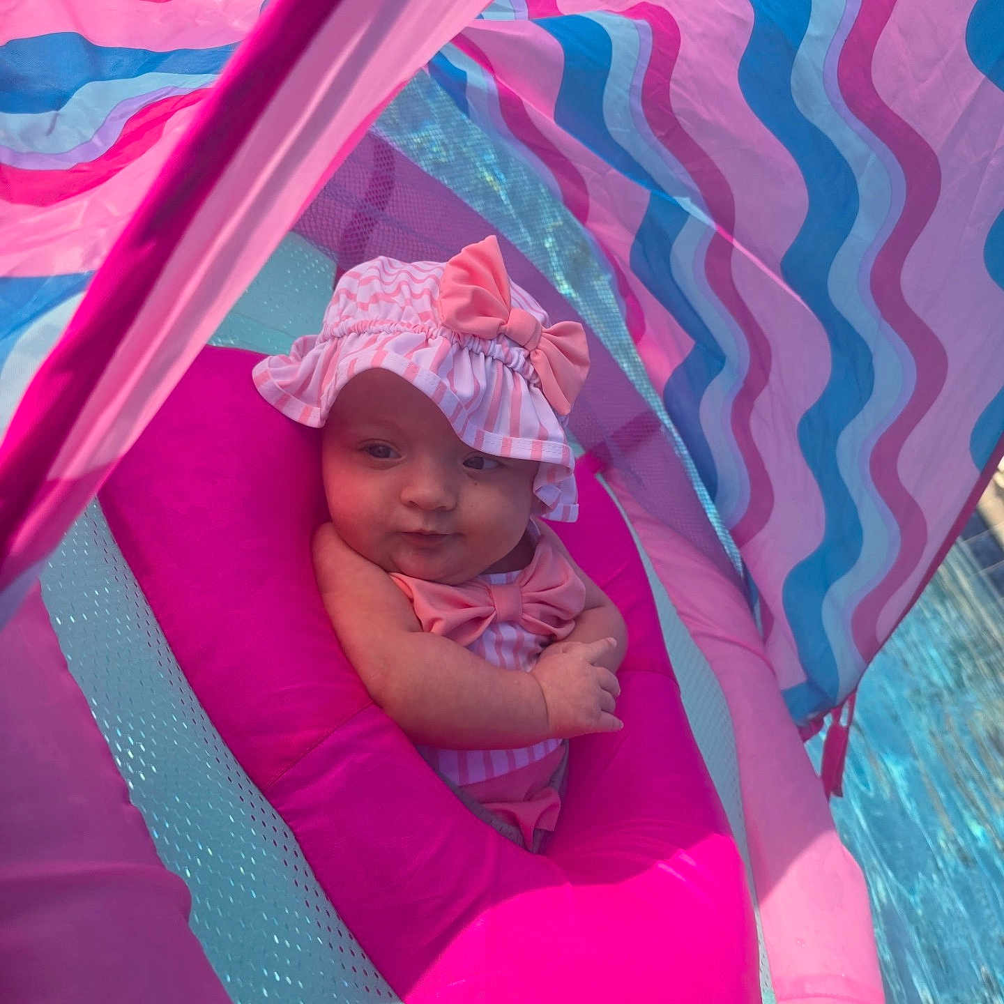 Izabella is registered to the contest to win money with this photo: baby, infant, pink, float, pool, water, hat, bow, swimming, child, outdoor, sunlight, colorful, striped, cute, relaxing, summer, portrait, closeup, fun