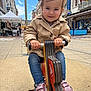 child, toddler, playground, spring_rocker, pink_shoes, pony_tails, jacket, jeans, outdoor, urban, street, buildings, sky, daytime, smiling, toy, person, fun, play, happy