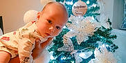 Benjamin is registered to the contest to win money with this photo: baby, child, christmas_tree, cute, decoration, face, festive, flower, green, hand, holiday, indoor, lights, ornament, pajamas, person, pine_tree, portrait, white, wooden_sign