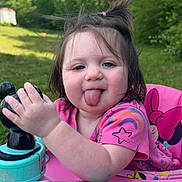 Scarlett is registered to the contest to win money with this photo: toddler, child, playful, tongue_out, pink_clothing, toy, walker, outdoor, greenery, grass, sunlight, hair_tie, baby_toy, happy, cute, portrait, summer, nature, fun, smiling