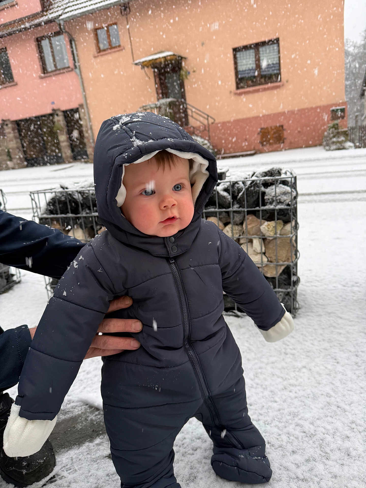 Yanis participe au concours pour gagner de l'argent avec cette photo : baby, infant, child, snow, winter, snowsuit, hood, mittens, outdoor, street, building, caged_rocks, standing, adult_hand, cold, portrait, rosy_cheeks, surprised, snowflake, coat