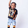 black_sneakers, black_tshirt, casual, child, confident, cute, denim_shorts, fashion, happy, isolated, joyful, orange_socks, portrait, pose, smiling, standing, studio, toddler, white_background, young_child
