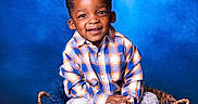 Semaj is registered to the contest to win money with this photo: basket, blue_background, braided_hair, casual_clothing, child, colorful, cozy, cute, fashion, fluffy_blanket, gray_sneakers, happy, indoor, person, plaid_shirt, portrait, sitting, smiling, studio, young_child
