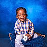 basket, blue_background, braided_hair, casual_clothing, child, colorful, cozy, cute, fashion, fluffy_blanket, gray_sneakers, happy, indoor, person, plaid_shirt, portrait, sitting, smiling, studio, young_child