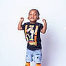 black_shoes, black_tshirt, casual_clothing, child, cute, denim_shorts, fashion, fun, happy, joyful, orange_socks, person, portrait, short_hair, smiling, standing, studio, toddler, victory_pose, white_background