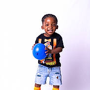 Semaj is registered to the contest to win money with this photo: black_shoes, black_tshirt, blue_ball, boy, casual_clothing, child, cute, denim_shorts, footwear, happy, indoor, orange_socks, playful, portrait, shorts, smiling, standing, studio, toddler, white_background