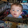 Mateo joined the competition — help win amazing prizes! baby, child, playpen, blue_eyes, indoor, person, furniture, shelf, clothing, pattern, animal_print, curly_hair, face, expression, toy, colorful, room, floor, person_in_background, baby_clothes
