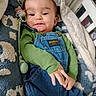 Mateo is registered to the contest to win money with this photo: baby, infant, child, denim_overalls, green_shirt, pacifier, blanket, crib, hand, face, smile, drool, clothing, indoor, cute, baby_gear, text_warning, fabric, comfort, portrait
