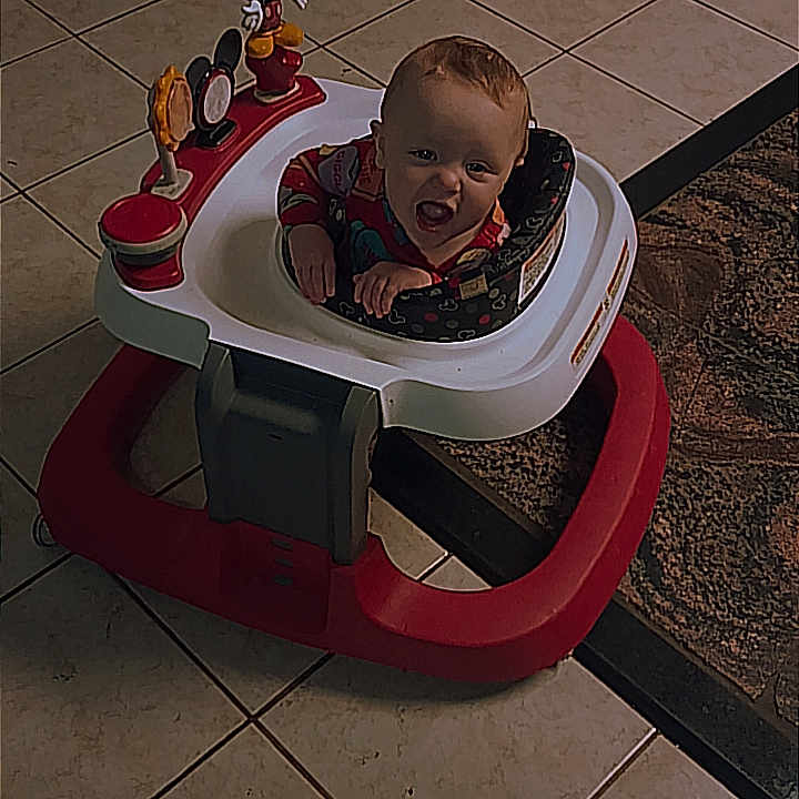 Kinleigh is registered to the contest to win money with this photo: baby, walker, toy, mickey_mouse, floor, tile, carpet, door, child, indoor, playtime, smiling, cute, furniture, person, home, floor_tiles, child_toy, infant, happy