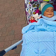 Yug Sanskar Ahuja is registered to the contest to win money with this photo: baby, blanket, blue, stroller, hat, toy, smile, child, outdoor, pavement, knit, colorful, pattern, pom_pom, cute, happy, person, infant, warm, cozy