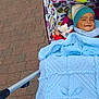 baby, blanket, blue, stroller, hat, toy, smile, child, outdoor, pavement, knit, colorful, pattern, pom_pom, cute, happy, person, infant, warm, cozy
