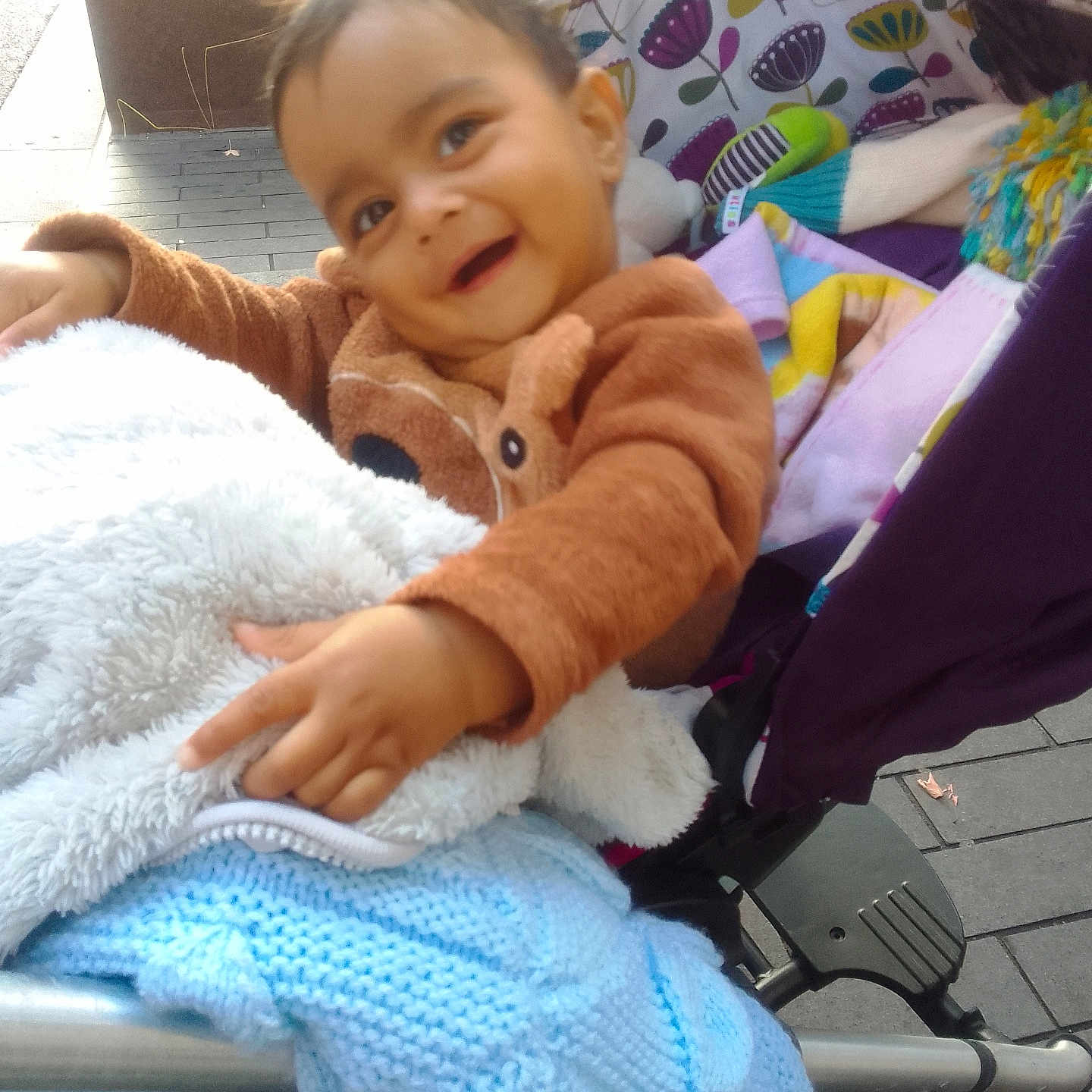 Yug Sanskar Ahuja is registered to the contest to win money with this photo: baby, blanket, child, colorful, cozy_clothing, fabric, happy, knitwear, outdoor, patterned, pavement, person, playful, pointing, seat, smiling, stroller, toddler, toy, warm
