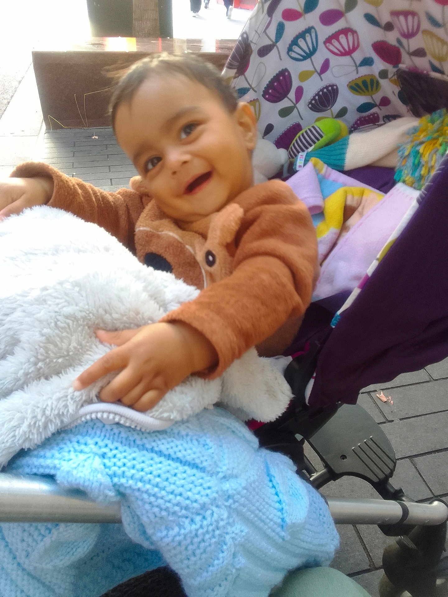 Yug Sanskar Ahuja is registered to the contest to win money with this photo: toddler, child, stroller, blanket, cozy_clothing, pointing, happy, smiling, outdoor, pavement, toy, knitwear, colorful, patterned, baby, person, playful, seat, fabric, warm