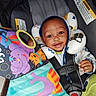 baby, car_seat, child, smiling, hood, neck_pillow, toy, book, colorful, clothing, seatbelt, infant, cute, happy, indoor, person, face, playful, cozy, safe