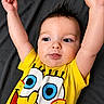 arms_up, baby, background, blue_eyes, cartoon_character, child, clothing, cute, expression, face, hair_spikes, indoor, infant, lying_down, person, playful, portrait, spongebob, tongue_out, yellow_shirt