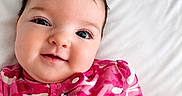 Harlie joined the competition — help win amazing prizes! baby, bed, camouflage_pattern, child, close_up, cute, expression, face, hair, happy, infant, lying_down, onesie, pink_clothing, portrait, skin, smile, soft_lighting, white_background, young_child