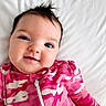 baby, bed, camouflage_pattern, child, close_up, cute, expression, face, hair, happy, infant, lying_down, onesie, pink_clothing, portrait, skin, smile, soft_lighting, white_background, young_child