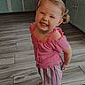child, toddler, smiling, pink_top, striped_skirt, sandals, kitchen, flooring, cabinet, window, happy, standing, indoors, hair_bow, wood_floor, tile_floor, cute, person, portrait, home