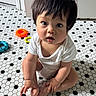baby, child, floor, tiles, white_clothing, sitting, indoor, toy, colorful, foot, hand, curly_hair, expression, looking_up, skin, playtime, cute, person, young_child, floor_pattern