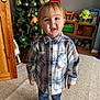 Tommy is registered to the contest to win money with this photo: toddler, child, indoor, plaid_shirt, christmas_tree, toys, carpet, striped_socks, smiling, furniture, wooden_door, playroom, holiday_decor, green_ornaments, buttoned_shirt, young_child, happy, home, portrait, casual_clothing