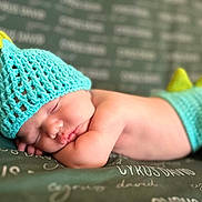 Cyrus joined the competition — help win amazing prizes! baby, sleeping, crocheted_hat, crocheted_shorts, dinosaur_costume, green_blanket, text, infant, cute, peaceful, soft_skin, closeup, resting, headwear, cozy, child, portrait, indoor, newborn, cute_costume