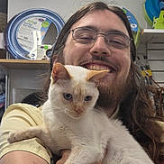 Biscuit joined the competition — help win amazing prizes! person, cat, smiling, glasses, long_hair, beard, white_cat, indoor, pet_store, shelf, pet_products, holding, happy, animal, feline, portrait, casual, friendly, cute, closeup