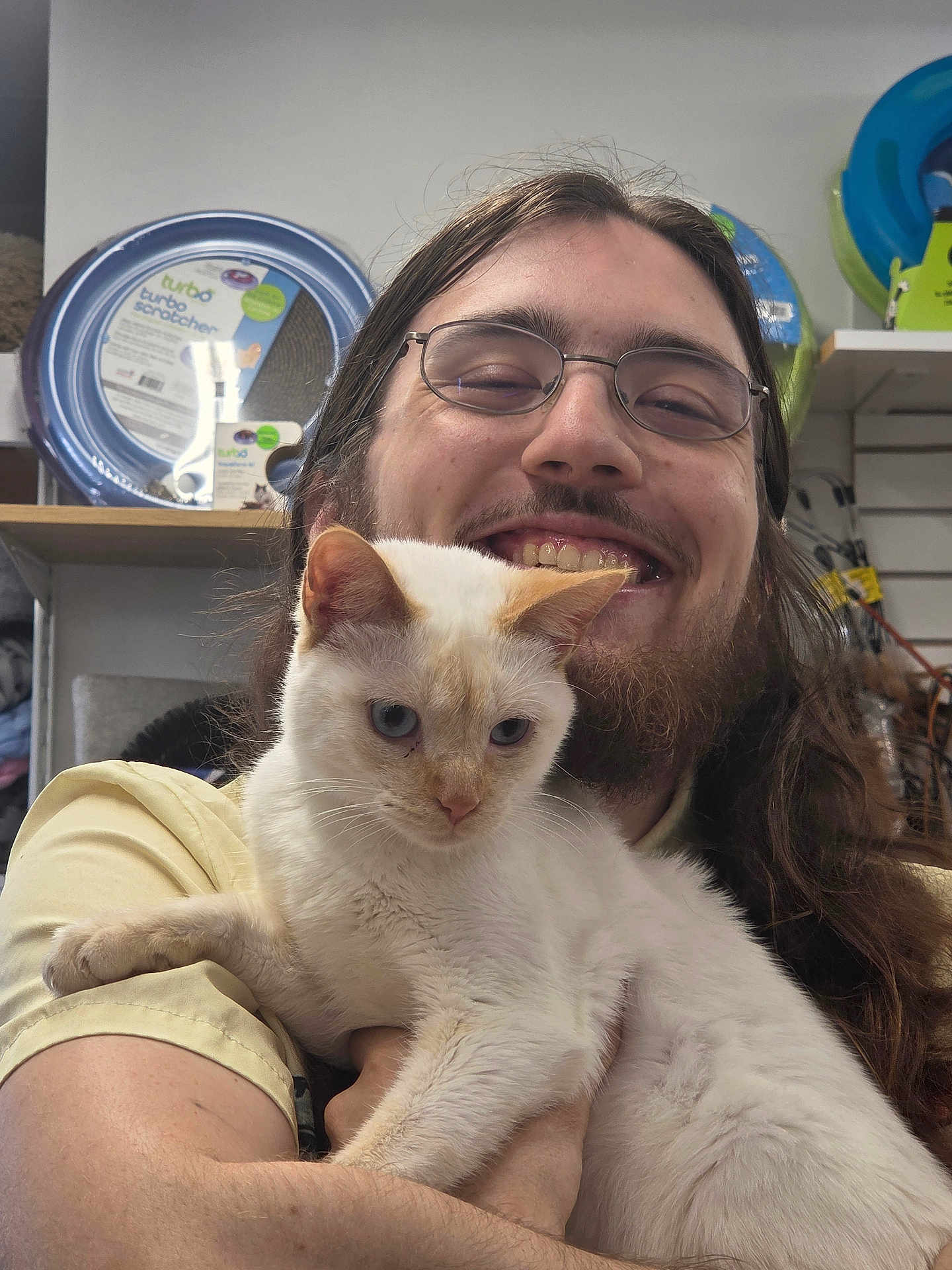 Biscuit joined the competition — help win amazing prizes! person, cat, smiling, glasses, long_hair, beard, white_cat, indoor, pet_store, shelf, pet_products, holding, happy, animal, feline, portrait, casual, friendly, cute, closeup