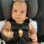 Vivian is registered to the contest to win money with this photo: baby, car_seat, graco, child, infant, seatbelt, straps, yellow_clothing, bow, face, hands, cute, secure, car_interior, young_child, sitting, looking_at_camera, blue_eyes, head_support, closeup