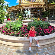 Yliana a rejoint le concours — aidez-le/la à gagner de superbes lots ! child, toddler, flowerbed, flowers, statue, bench, outdoor, daylight, building, sky, greenery, playful, smile, pavement, shoes, casual_clothing, sculpture, amusement_park, park, sunlight