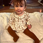 Violette is registered to the contest to win money with this photo: baby, child, infant, headband, bow, dress, tights, sitting, blanket, indoor, floor, curly_hair, cute, portrait, smile, person, young_child, warm_lighting, cozy, floor_rug