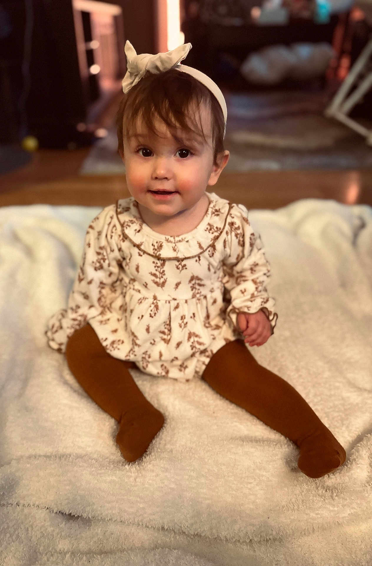 Violette is registered to the contest to win money with this photo: baby, child, infant, headband, bow, dress, tights, sitting, blanket, indoor, floor, curly_hair, cute, portrait, smile, person, young_child, warm_lighting, cozy, floor_rug