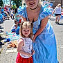 child, woman, princess_costume, blue_dress, red_skirt, unicorn, smile, outdoor, parade, crowd, american_flag, street, daylight, happy, people, event, young_girl, costume, celebration, public