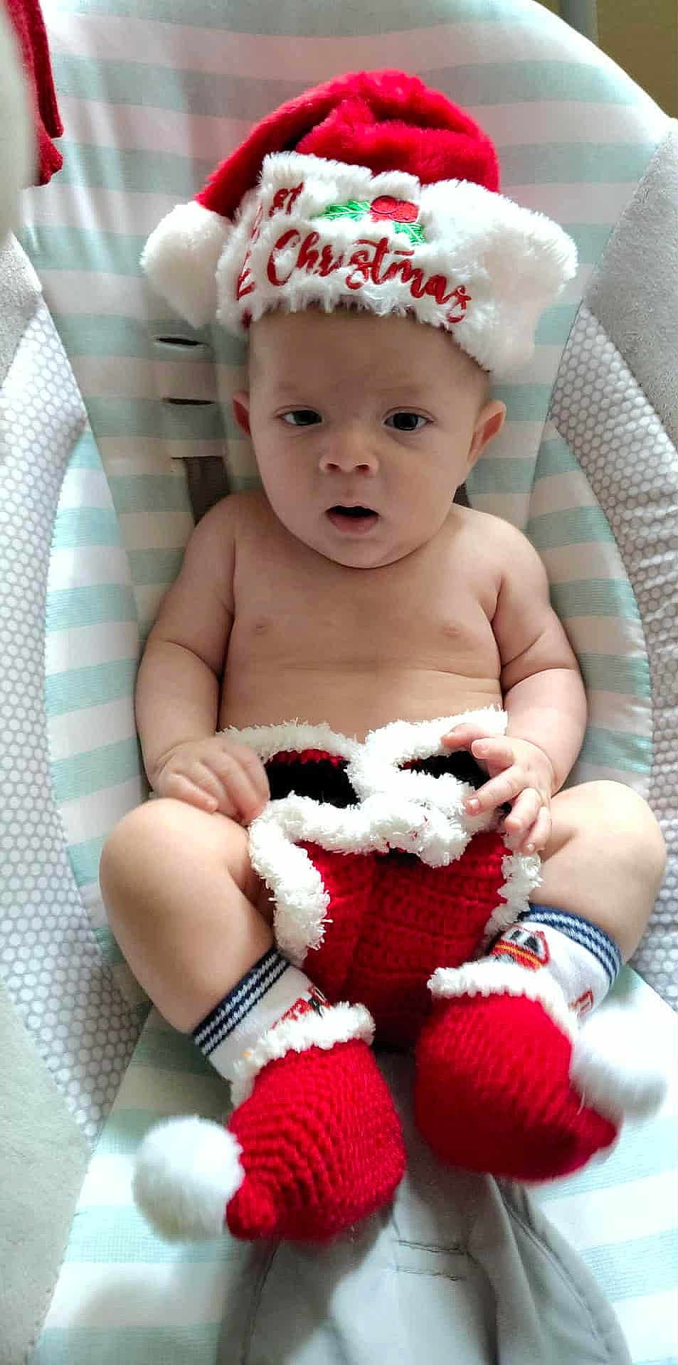 William is registered to the contest to win money with this photo: baby, child, christmas_hat, knitted_booties, baby_seat, striped_pattern, dotted_pattern, festive_clothing, infant, cute, holiday, red, white, soft_toys, portrait, indoors, sitting, curious, face, skin