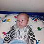 baby, infant, child, blanket, pillow, duck_pattern, onesie, striped_sleeves, animal_print, bed, sleeping_area, cute, indoor, face, head, hands, young_child, soft_texture, lying_down, looking_away
