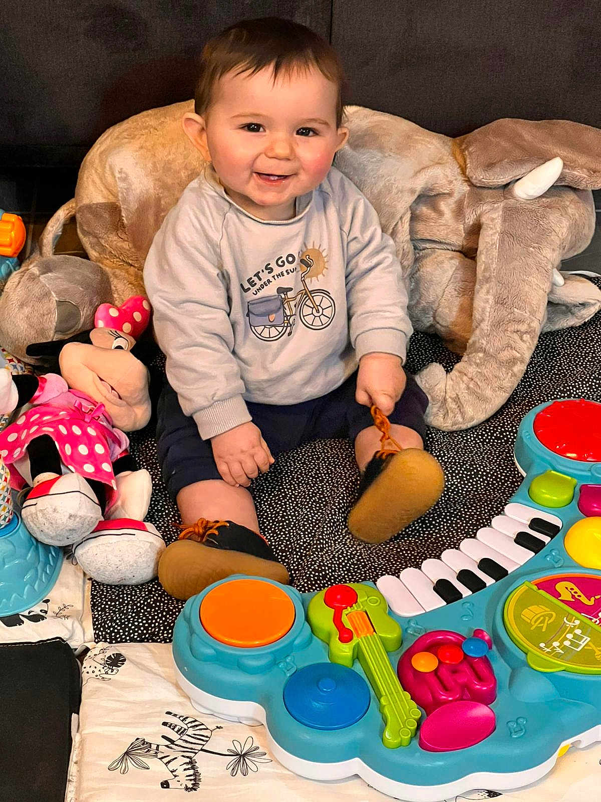 Alexandre a rejoint le concours — aidez-le/la à gagner de superbes lots ! baby, child, smiling, sitting, toy, plush_elephant, stuffed_animal, minnie_mouse, sweatshirt, shoes, playmat, colorful, indoor, cute, happy, face, person, infant, floor, fun