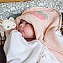 baby, towel, hood, plush_toy, bunny, face, infant, blanket, pattern, animal_print, cute, soft_texture, gaze, child, bed, rest, comfort, pink, white, portrait